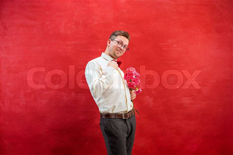 Young beautiful man with flowers on red studio background, stock photo