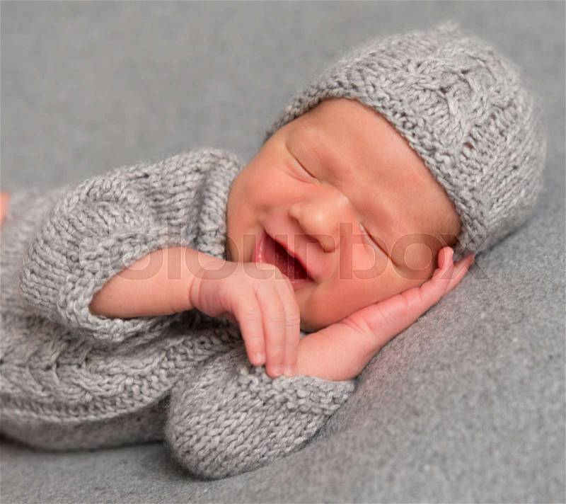 Pure emotions of a smiling baby in a knitted hat asleep, closeup, stock photo