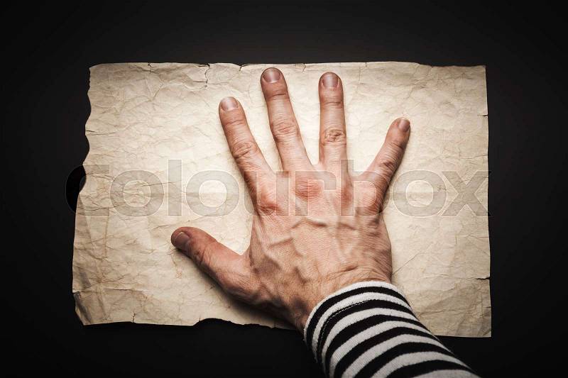 Strong sailors hand covers empty old crumpled paper sheet over black background, pirate map copy-space template, stock photo
