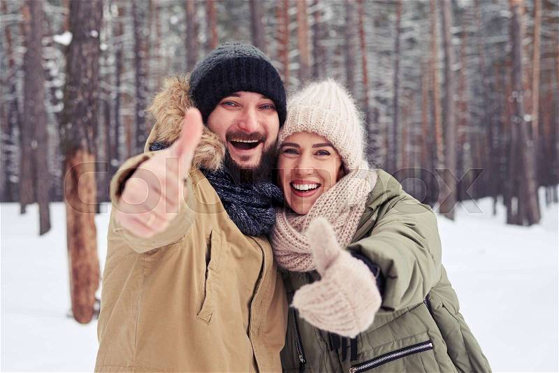 Close-up of smiling couple snowing thumbs up gesture and hugging on a cold winter weather. The concept of togetherness and happy family , stock photo