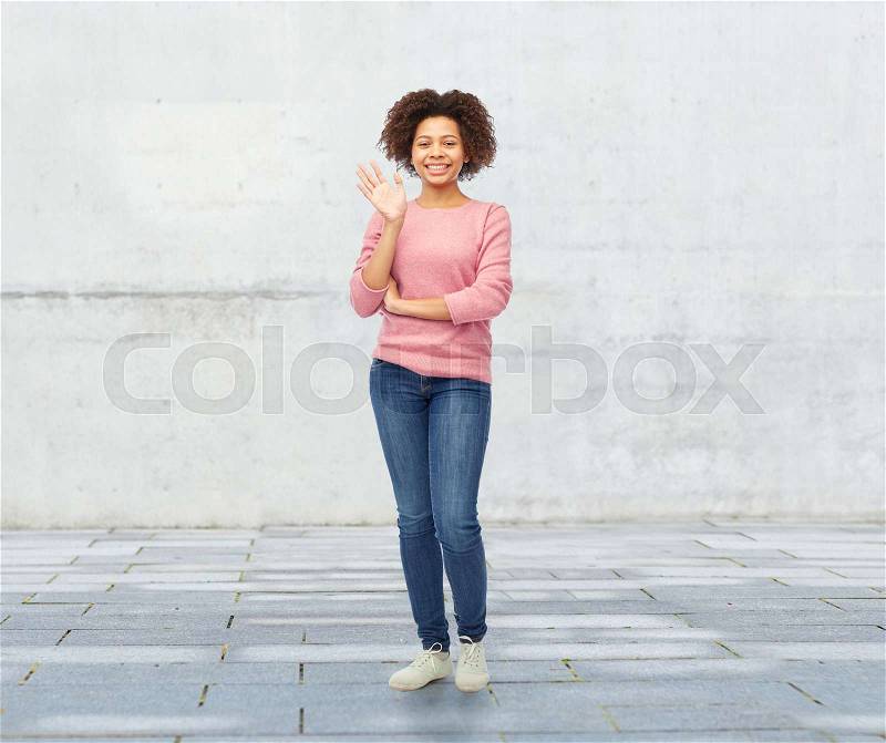 People, race, ethnicity and gesture concept - happy african american young woman waving hand over stone wall background, stock photo