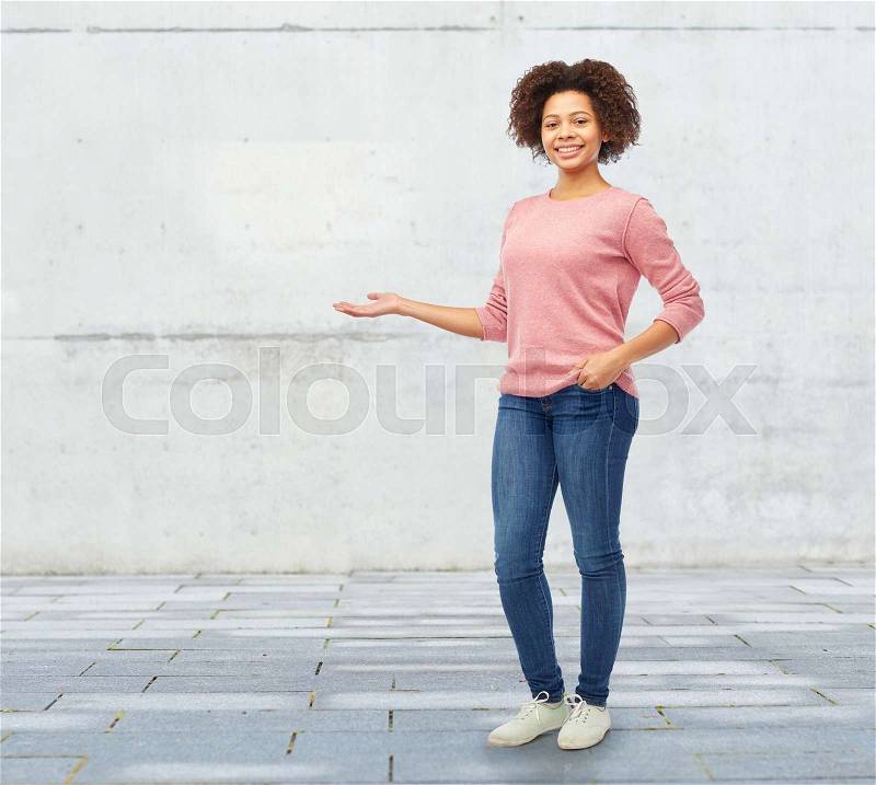 People, race, ethnicity and portrait concept - happy african american young woman holding something imaginary on hand over stone wall background, stock photo