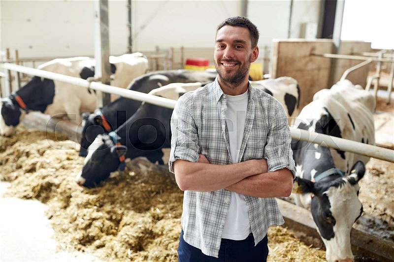 Agriculture industry, farming, people and animal husbandry concept - happy smiling young man or farmer with herd of cows in cowshed on dairy farm, stock photo