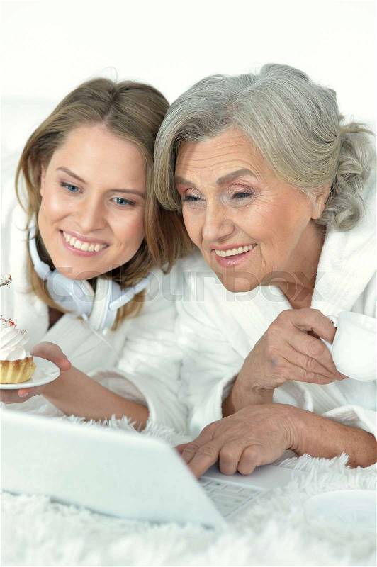 Portrait of senior woman with her adult daughter eat tasty cake, dring tea and watching something on laptop, stock photo
