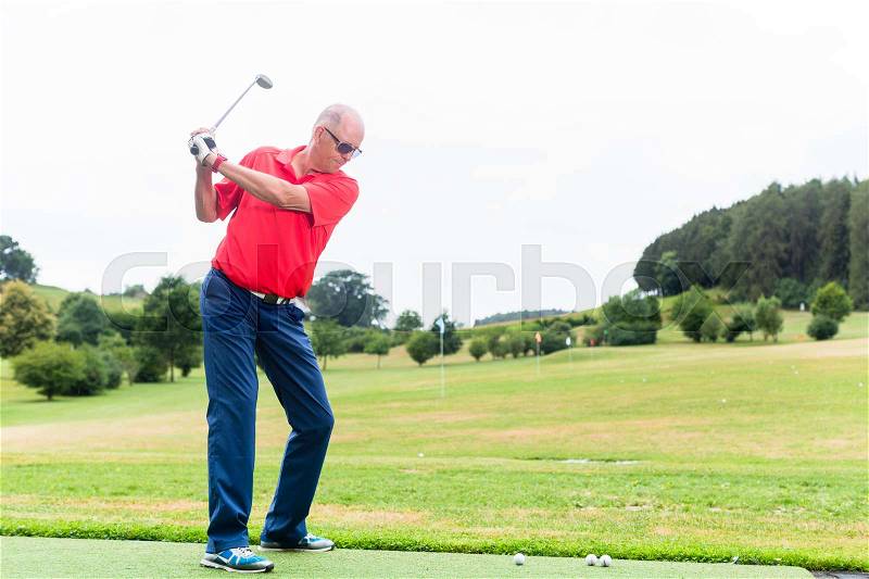 Golfer training his swing on golf driving range, stock photo