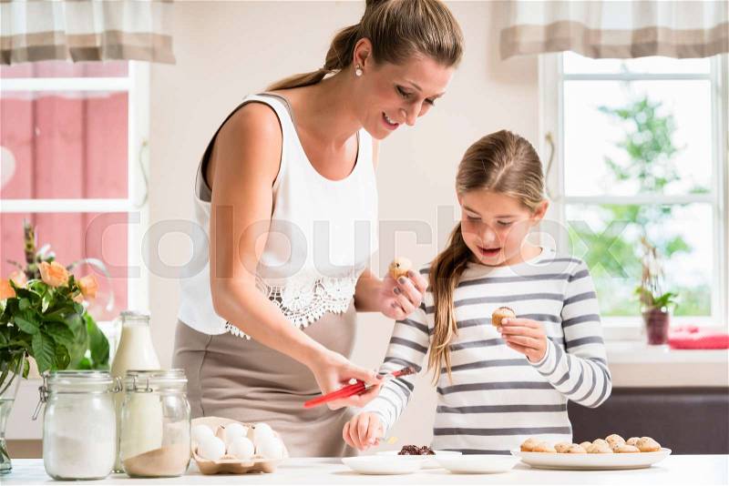 Pregnant mum and her little daughter baking together and decorating the cupcakes, stock photo