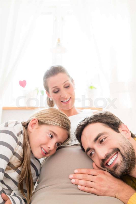 Girl and dad listening at moms belly for soon-to-be sibling, stock photo