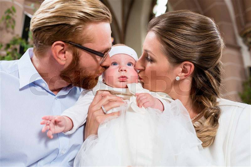 Young parents kiss their baby at the same time after the christening ceremony, stock photo