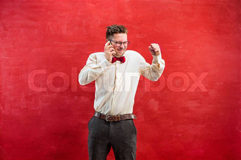 Portrait of puzzled man in glasses talking by phone on a red studio background, stock photo