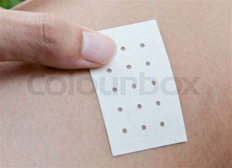 Human hand is sticking the menthol plaster to skin, stock photo