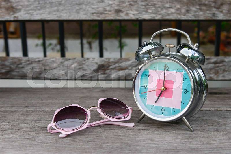 Pink sunglasses and alarm clock on the wooden table, stock photo