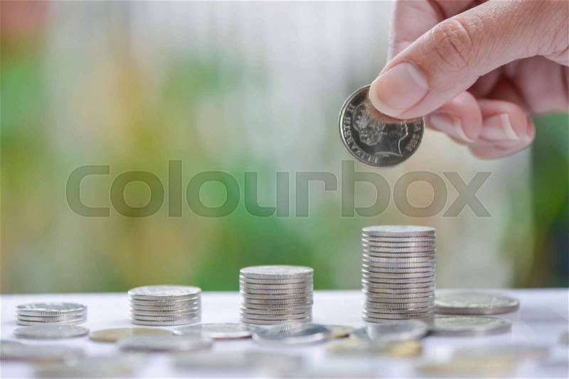 Woman hand putting coin to growing coins stacks - Concept of saving money, stock photo