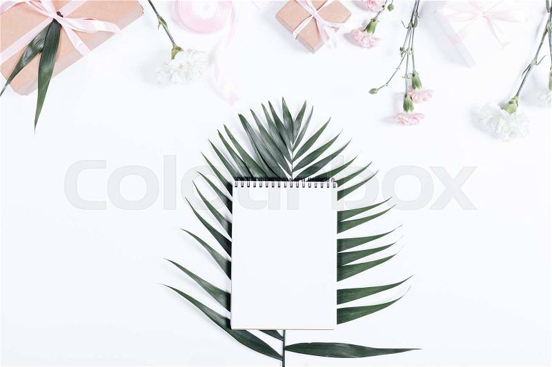 Holiday composition: notebook, boxes with gifts, ribbons and flowers lie on a white table top view, stock photo