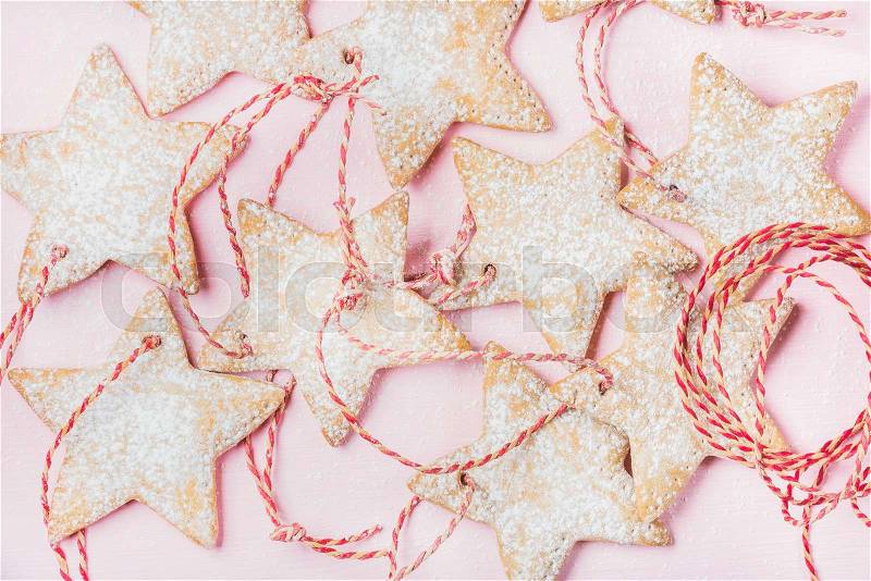 Close-up of Christmas homemade gingerbread star shaped cookies with sugar powder and red decoration rope over light pink background, top view, horizontal composition, stock photo