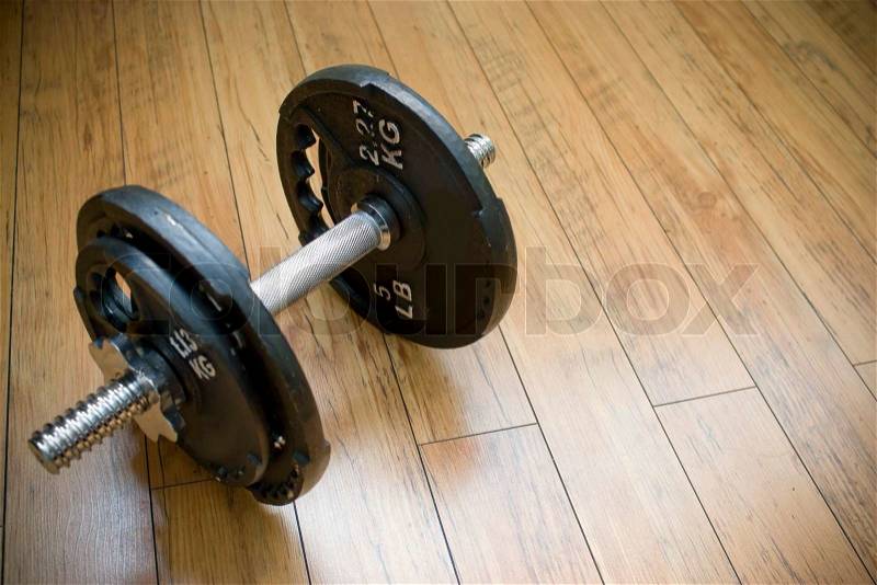A free weight dumbell sitting on a wood floor - the perfect accessory to any home gym, stock photo