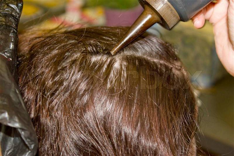 A closeup of a woman getting hair dye applied to her scalp, stock photo