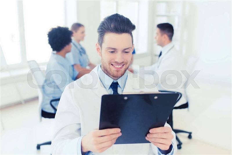 Clinic, profession, people and medicine concept - happy male doctor with tablet pc computer over group of medics meeting at hospital, stock photo
