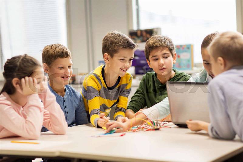 Education, children, technology, science and people concept - group of happy kids with laptop computer building robots at robotics school lesson, stock photo