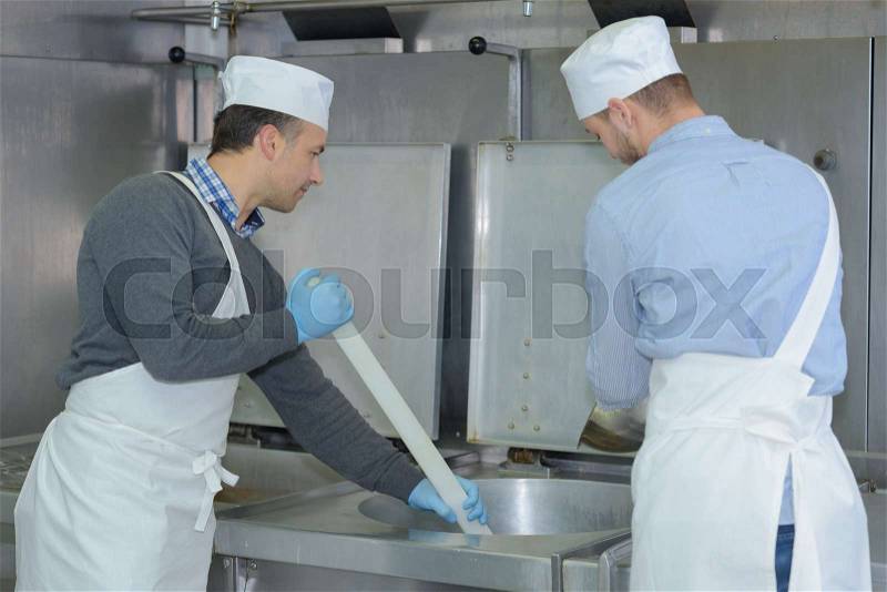 Apprentice and chief preparing meat in restaurant kitchen, stock photo