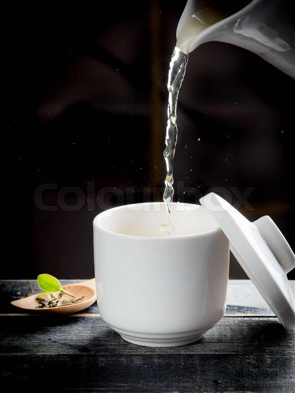 Green tea pouring into tea cup on dark wooden backgroud, stock photo