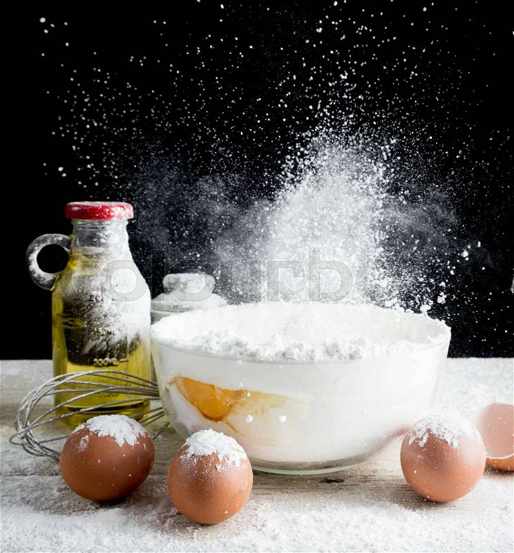 Baking Ingredients (eggs,flour,olive oil) on table wood,Flying flour, stock photo