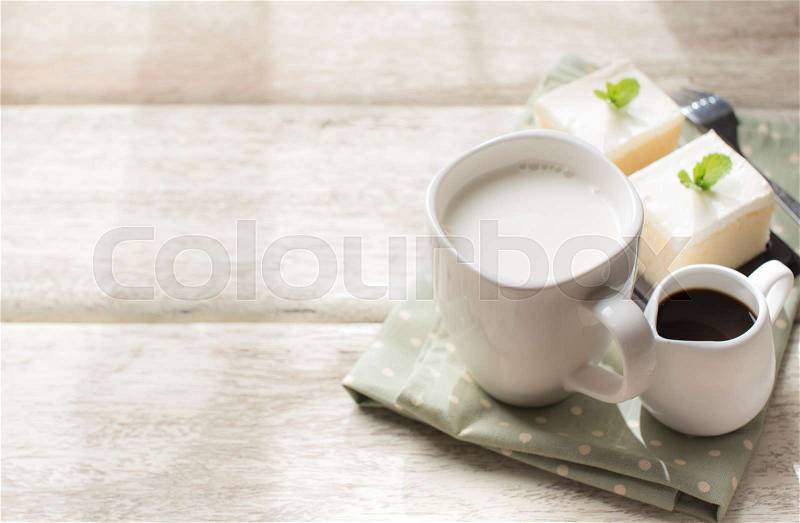 Glass of milk and milk cake delicious on the wood table with shadows from a window frame, stock photo