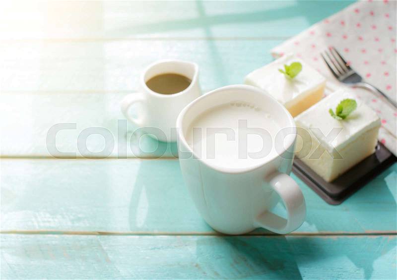 Glass of milk and milk cake delicious on the wood table with shadows from a window frame, stock photo
