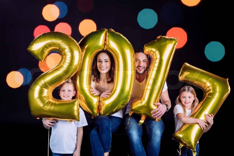 Happy family holding golden 2017 sign balloons and looking at camera on black, stock photo