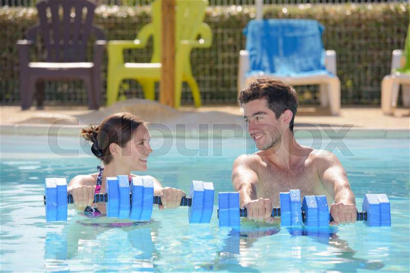 Man and woman holding floats in swimming pool, stock photo
