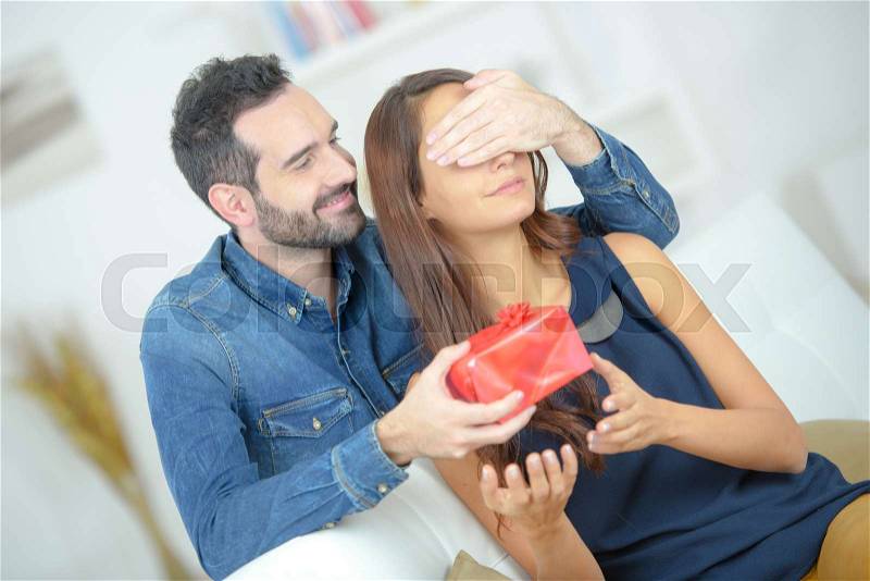 Young attentive man offering gift to his beloved girlfriend, stock photo