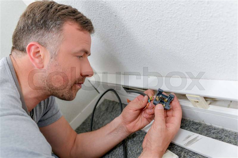 Man fitting electrical socket in skirting board, stock photo