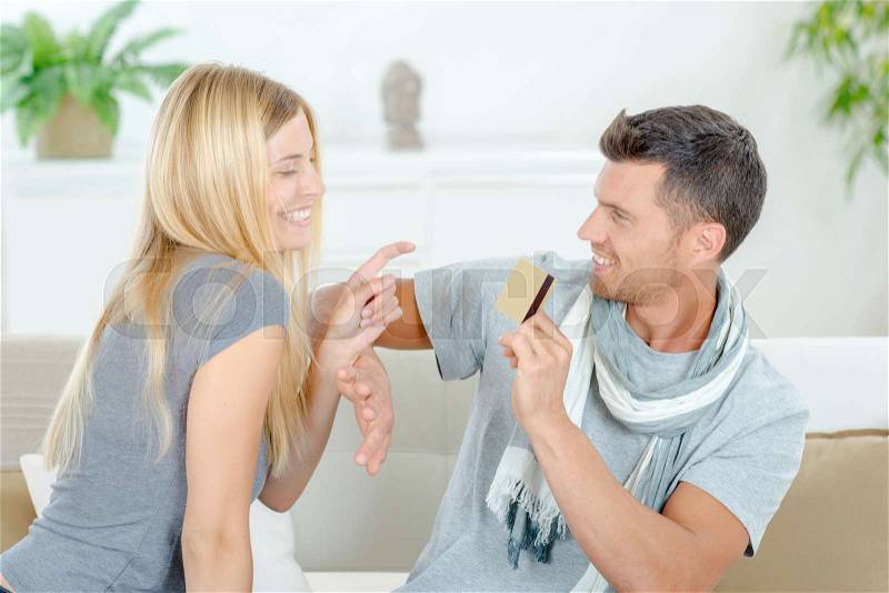 Couple on sofa, man withholding credit card, stock photo