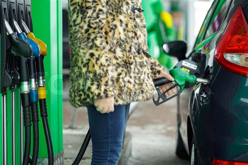 Woman fills petrol into her car at a gas station in winter closeup, stock photo