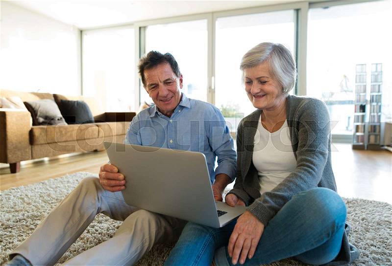 Beautiful senior woman and man sitting on the floor in living room, working on laptop, stock photo