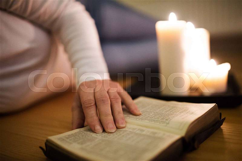 Unrecognizable woman lying on the floor reading her Bible. Burning candles next to her. Close up of the book and her hand, stock photo