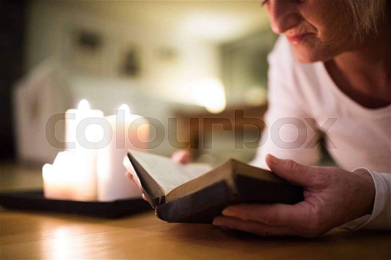 Unrecognizable woman lying on the floor reading her Bible. Burning candles next to her. Close up, stock photo