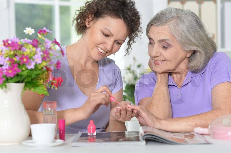 Daughter making manicure to her mother, painting nails, stock photo