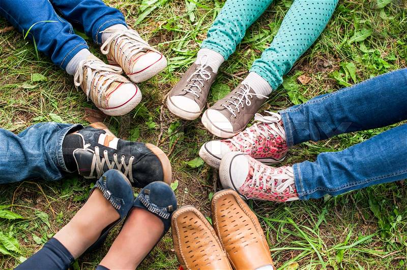 A group of friends sitting on the green grass make foot circle with their legs adn different shoes. Selective focus, top view, stock photo