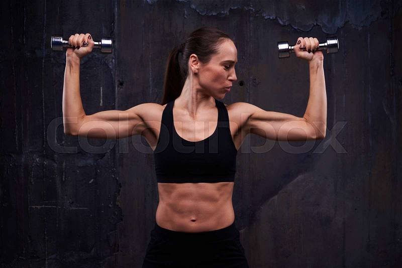 Close-up of muscular female doing biceps curl with dumbbells. Strength workout of muscular confident female doing biceps curl with dumbbells. Showing her pumped biceps, triceps and press, stock photo