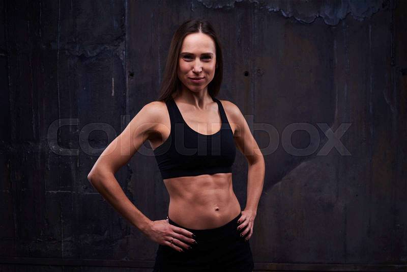 Close-up of half-turned sportswoman with hands on waist looking at the camera isolated in studio. Confident muscular woman showing the relief of abdomen, stock photo