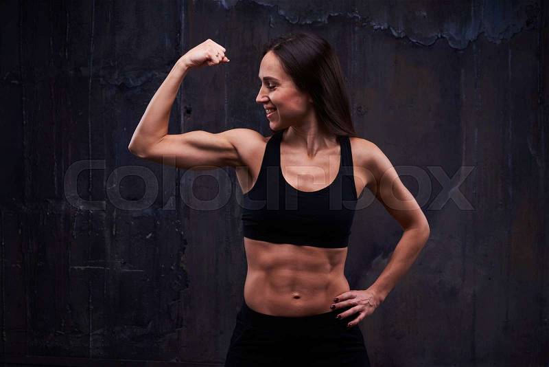 Close-up of cheerful woman in the studio, showing biceps. Woman with perfect biceps and triceps demonstrating muscles. The concept of sport and healthcare , stock photo