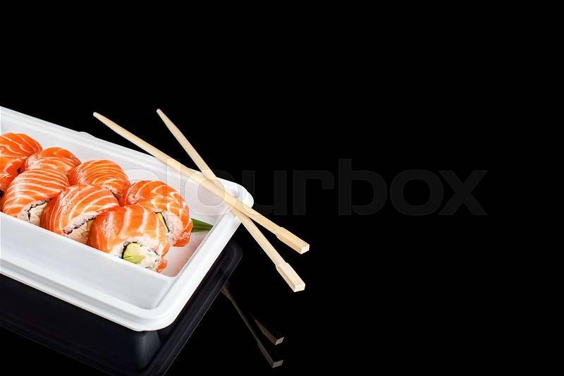 Sushi rolls made of fresh raw salmon, cream cheese and avocado in white plastic container ready to eat on black background with reflections. Free space for text, stock photo