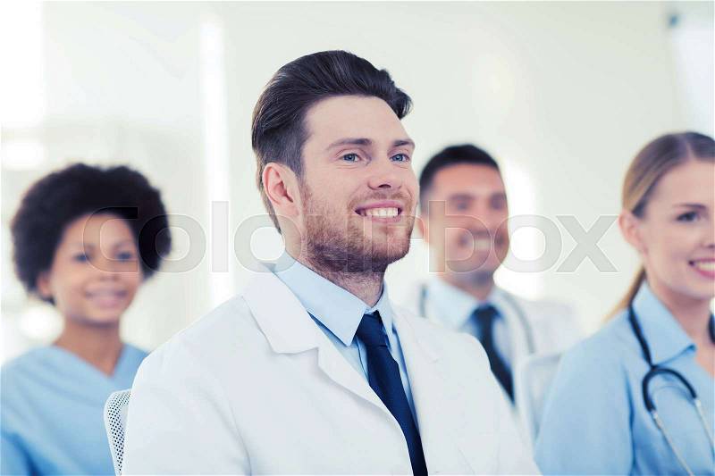 Clinic, profession, people and medicine concept - happy male doctor over group of medics meeting at hospital, stock photo