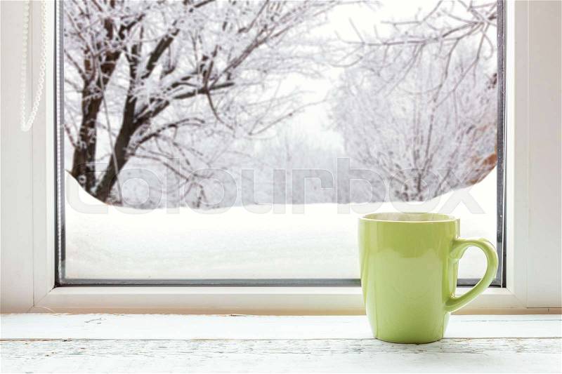 Cup of coffee on the window sill. In the background, a beautiful winter landscape in snow. Cozy home concept, stock photo