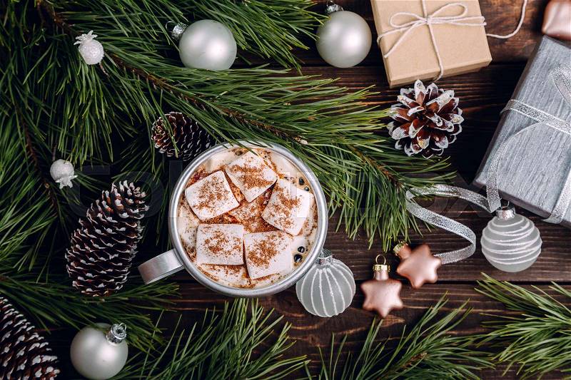 Cup of white marshmallows on the dark brown wooden table with fir branches, cones, balls, gifts and New Year decorations, cozy Christmas background, top view, stock photo