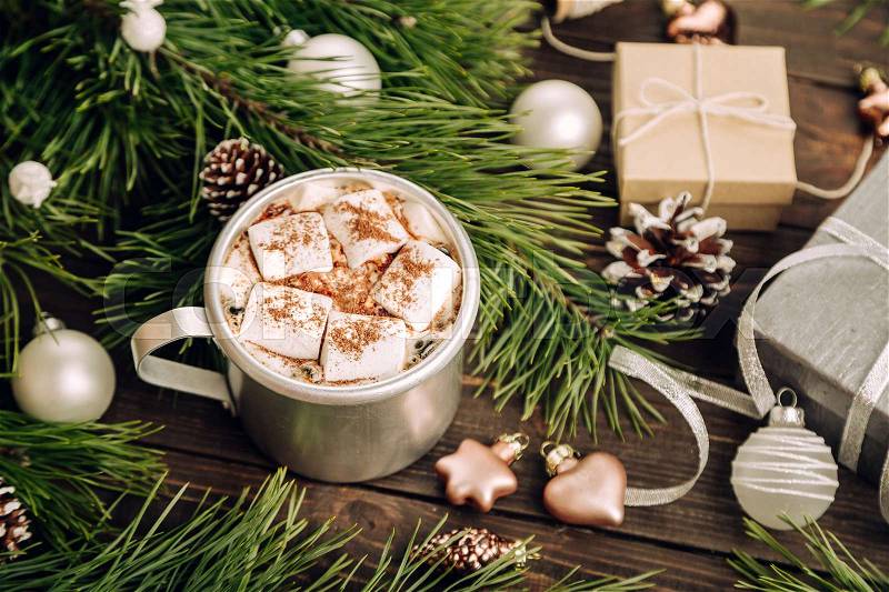 Cup of marshmallows on the dark brown wooden table with fir branches, cones, balls, gifts and New Year decorations, cozy Christmas background, top view, stock photo