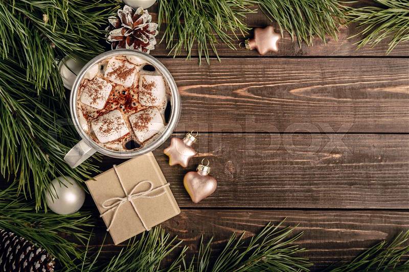 Cup of white marshmallows on the dark brown wooden table with fir branches, cones, balls, gifts and New Year decorations, cozy Christmas background, top view, copy space at the right, stock photo
