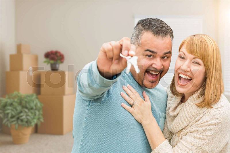 Mixed Race Couple Holding House Keys Inside Empty Room with Moving Boxes, stock photo