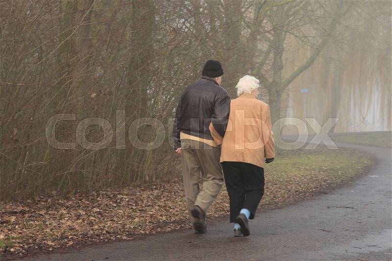 Old retired couple, man and wife are walking in the misty forest in the park at the country side in the soft winter, stock photo