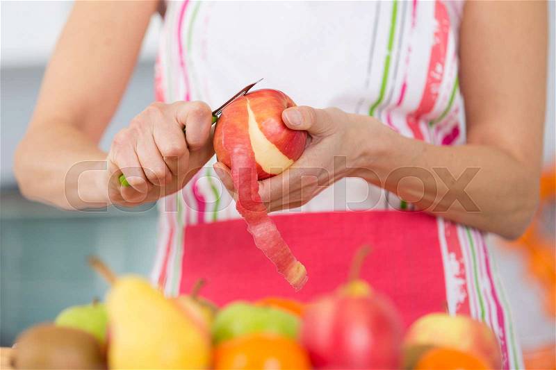 Elder woman peeling apples in her kitchen, stock photo